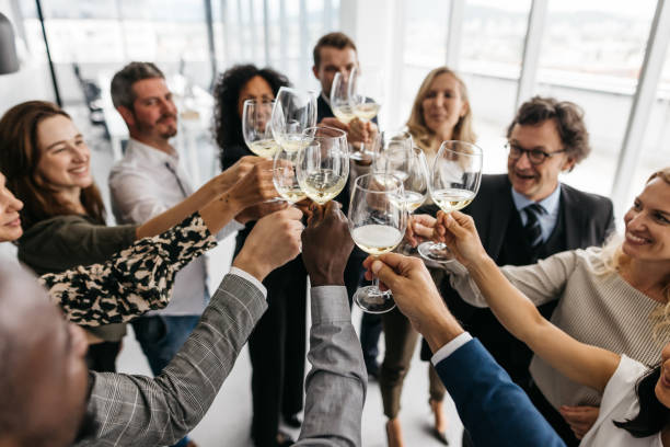 A photo of co-workers giving a toast with champagne in a bright office. They are smartly dressed and have a great time. Horizontal daylight indoor photo.